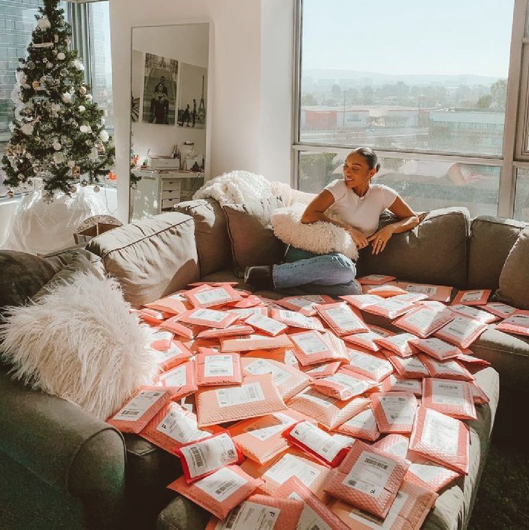 A woman sits on a couch surrounded by ready-to-ship packages with thermal printed shipping labels, printed with the Prafia Flex USB Label Printer. Ideal for e-commerce and online stores.